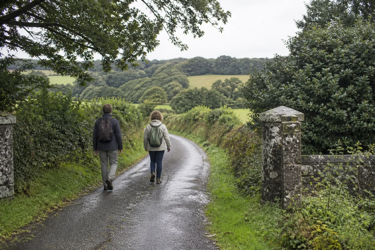 Deux marcheurs suivent une petite route humide entre les haies du bocage